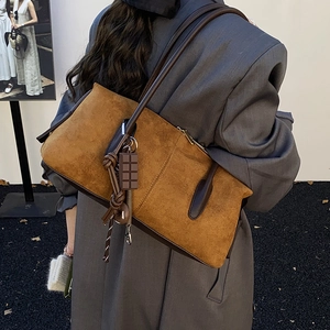 Brown suede shoulder bag with minimalist design and decorative charm shown on model back