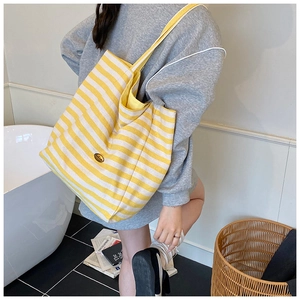 Close-up of a large yellow and white striped canvas tote bag with gold logo detail