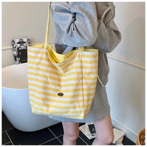 Detail of yellow and white striped canvas tote bag with an oval metal plaque