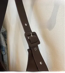 Détail de la bandoulière en cuir marron avec œillets métalliques et boucle carrée