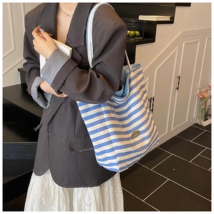 Detail of blue striped canvas tote bag featuring an oval handmade metal brand tag
