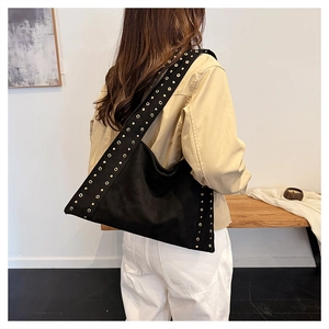 Close-up of black velvet shoulder bag with golden metal grommets on a female model