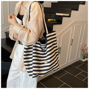 Close-up of black and white striped tote bag with oval gold metal emblem and woven straps