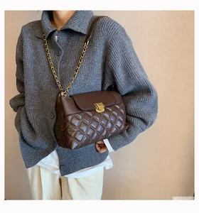 Détail du sac bandoulière matelassé marron foncé avec fermoir doré sur un mannequin