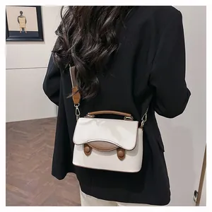 Détail d'un sac bandoulière beige avec bordures marron sur un blazer noir