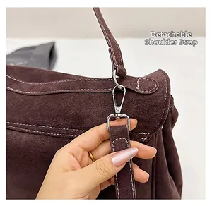 Detail of detachable shoulder strap with silver buckle and white stitching on suede bag