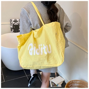 Détail d'un grand sac cabas en nylon jaune avec logo aiditu porté par un modèle