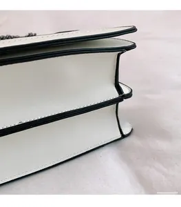 Detail of white leather crossbody bag showing accordion side gussets and black chain strap