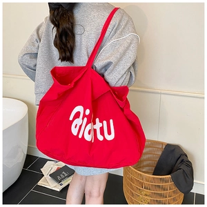 Détail du grand sac cabas en toile rouge avec lettrage blanc porté à l'épaule décontracté