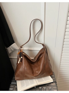 Détail d'un cabas vintage en cuir marron avec charme en perles de bois sur une valise