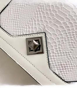 Close-up of white snake skin texture and metallic square lock on a stylish handbag