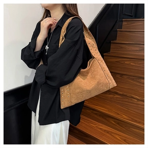 Brown suede shoulder bag with metal eyelets detail shown on a model by a wooden staircase