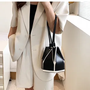 Detail of minimalist black and white geometric bucket bag held by model in white suit