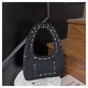Détail du sac bandoulière en daim noir avec clous argentés sur une chemise blanche