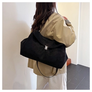 Detail of black matte suede shoulder bag with silver buckle and thin strap on a model