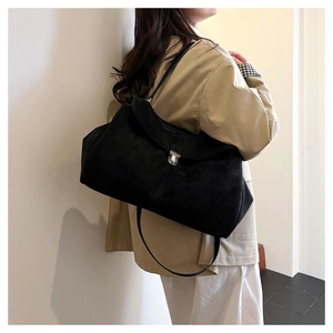 Detail of minimalist black suede tote bag featuring a round silver clasp and slim strap