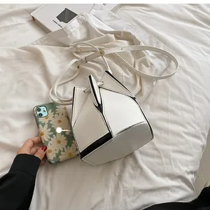 Size comparison of white geometric bucket bag next to a mobile phone on fabric