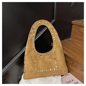 Détail du sac à main en daim marron avec des clous métalliques sur la poignée courbe