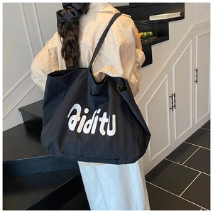 Détail d'un grand sac cabas noir en toile avec lettrage blanc et bandoulière large