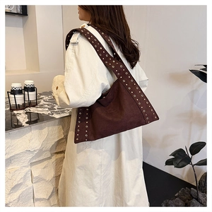 Detail of dark brown suede tote bag with metallic eyelet studs and wide shoulder strap