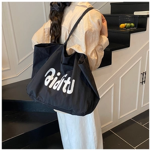 Détail d'un grand sac cabas en toile noire avec lettrage aidit blanc sur la bandoulière