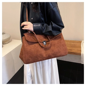 Detail of a brown suede shoulder bag with a silver buckle worn by a model