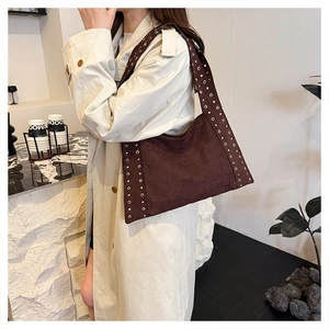 Detail of dark brown suede shoulder bag featuring decorative metallic eyelets and studs