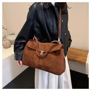 Brown suede shoulder bag with silver buckle worn by a model in a minimalist setting