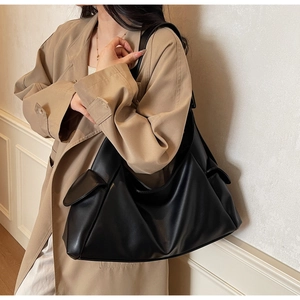 Detail van een grote zwarte minimalistische hobo schoudertas gestyled met een beige trenchcoat