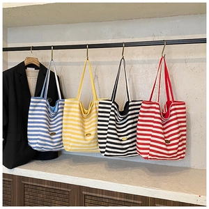 Row of striped canvas tote bags in four colors hanging on a rack with a blazer
