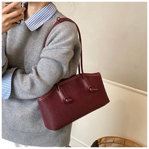 Close-up of burgundy woven leather tote featuring decorative knotted shoulder strap detail