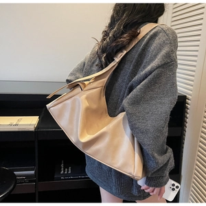 Detail van de minimalistische beige leren hobo-tas gedragen door een model in trui