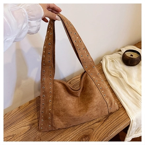 Detailed view of a brown velvet shoulder bag with golden rivets on a wooden table