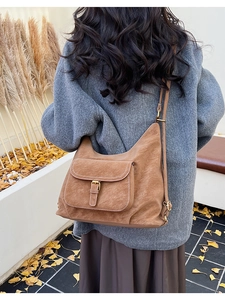 Détail d'un sac besace en daim marron avec coutures blanches et boucle en métal doré