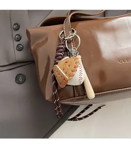 Close-up of baseball glove and bat keychain accessory hanging on a brown leather bag