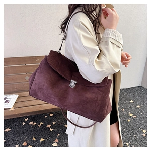 Close-up of burgundy suede shoulder bag featuring a metallic buckle and textured finish