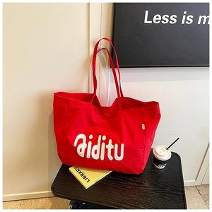 Détail du grand sac cabas rouge en toile avec texte blanc Aiditu sur une petite table