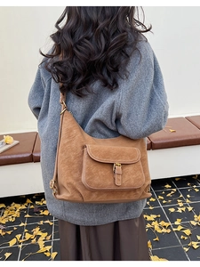 Sac à bandoulière en suédine marron avec poche à boucle porté sur un manteau gris