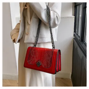 Detailed view of red leather crossbody bag with snake skin texture and metal chain
