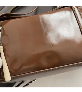 Detail of coffee leather underarm bag featuring embossed CLEAROK logo and baseball bat charm