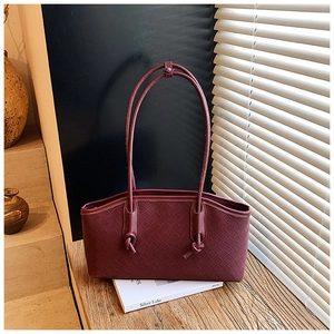 Close-up of burgundy woven leather tote bag with knotted handles on wooden table