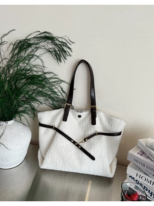 Close-up of white plush tote bag with brown faux leather straps and buckle detail