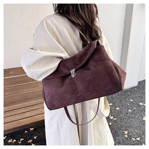 Detailed view of brown suede shoulder bag with silver metal lock on beige trench coat
