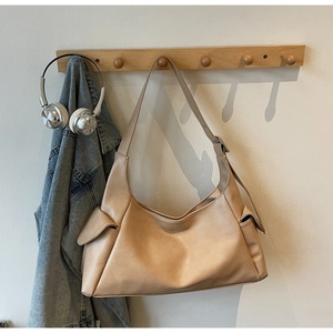 Detail van de beige hobo-tas met zijzakken en schouderband aan een houten kledinghanger