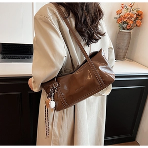 Detailed view of deep brown glossy tote bag with stylish charms worn by a model