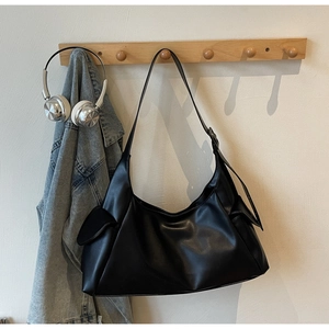 Detail van zwarte hobo tas met zijvak hangend aan een minimalistische houten haak