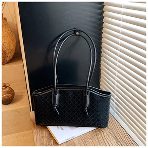 Detailed view of black woven leather texture and knotted strap on large shoulder bag