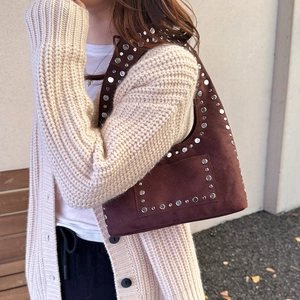 Sac sous le bras en daim marron avec rivets argentés posé sur un banc en bois