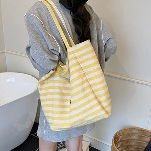 Minimalist yellow and white striped knit tote bag worn by a model in a modern bathroom