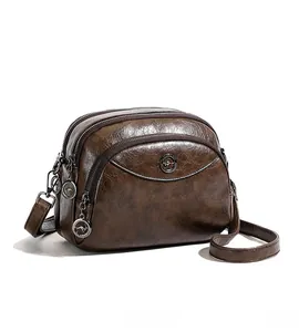 Detail view of the brown soft leather handbag showing three zippered compartments and logo